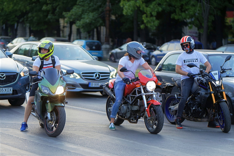23 - Three motorcyclists waiting at a street intersection alongside urban traffic